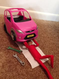 a pink toy car sitting on top of a floor next to scissors and a pair of pliers