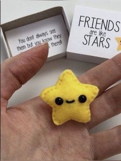 a hand is holding a small yellow star brooch with black eyes and two cards in the background