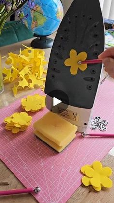 a person cutting paper with a large iron on top of it and yellow flowers in the background