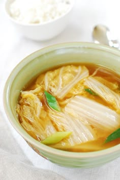 a green bowl filled with soup on top of a white cloth next to a spoon