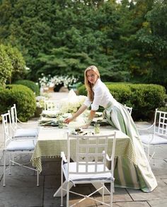 a woman is setting a table outside with white chairs and green cloths on it