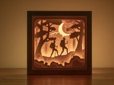 an illuminated shadow box with a silhouette of two people walking in the woods at night