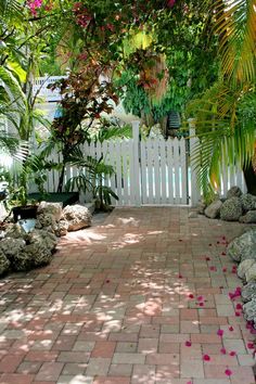 the walkway is lined with pink flowers and palm trees in front of a white picket fence