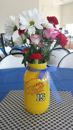 a yellow mason jar filled with flowers sitting on top of a blue tablecloth covered table