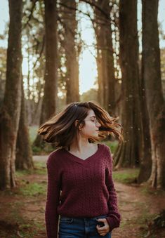 a woman standing in the woods with her hair blowing in the wind and looking up