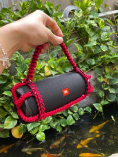 a hand is holding a red and black speaker in front of some water with goldfish