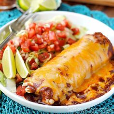 a white plate topped with enchilada covered in sauce next to a salad