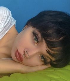 a woman laying on top of a green bed next to a blue wall with piercings