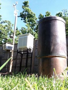 a large metal barrel sitting in the grass next to a wooden fence and some trees