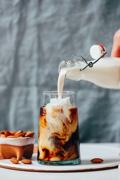 a person pouring milk into a glass filled with ice and nuts on a white table