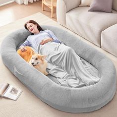 a woman laying on top of a dog bed next to a brown and white dog