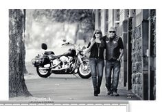 a man and woman walking down the street next to a motorcycle