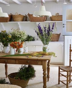 a wooden table topped with lots of flowers next to baskets filled with plants on top of shelves