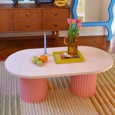 a table with flowers and fruit on it in front of a blue dresser, next to a mirror