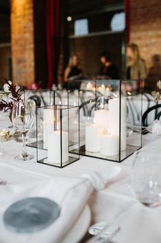 candles are placed in glass cubes on the table at a wedding reception with white flowers and greenery