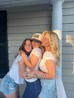 three young women hugging each other on the front porch of a house with blue shutters