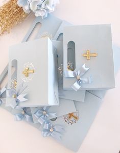 three blue boxes with gold crosses and bows on them sitting next to some paper flowers