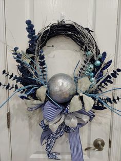 a wreath with blue and white decorations hanging on a front door, next to a silver ball