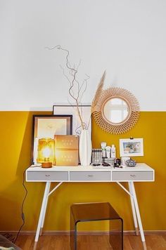 a white table with some pictures and a mirror on top of it next to a yellow wall