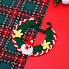 a crocheted christmas wreath on top of a plaid table cloth next to an ornament