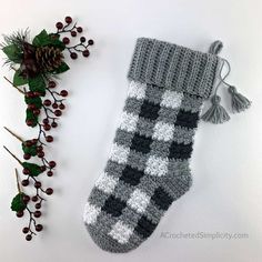 a knitted christmas stocking next to holly branches