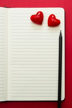 two red hearts are placed on top of a notepad next to a black pen