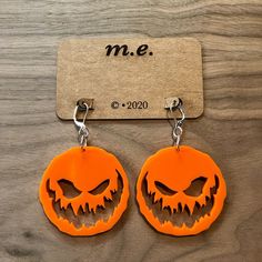 two orange earrings with carved pumpkin faces are on a wooden table next to a name tag