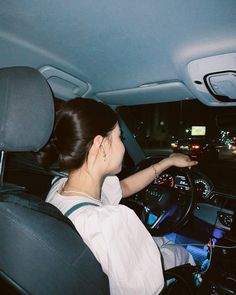 a woman sitting in the driver's seat of a car with her hand on the steering wheel