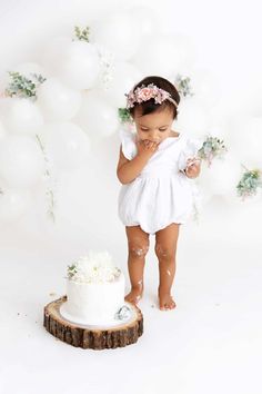 a baby girl standing in front of a white cake with flowers on it's head