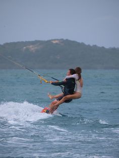 a man and woman riding on the back of a surfboard in the ocean while being pulled by a kite