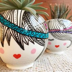 two white vases with designs on them and a plant in the middle one has a blue ribbon around its neck