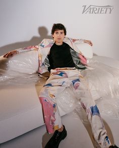 a young man sitting on top of a white couch covered in plastic wrapper next to a wall