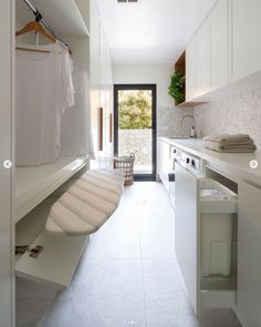 a white kitchen with an open door leading to another room that has clothes on hangers