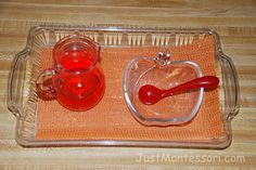 a glass tray with two cups and a red spoon on it, sitting on top of a wooden table