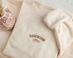 Embroidered Bookworm Sweatshirt Stay cozy and fun with our uniquely embroidered sweatshirt! Made with love and THOUSANDS of threads! -Unisex Size (Please see the size chart for more details that can be found in the photos section)  We recommend comparing your favorite sweatshirt to our size chart to find the best size for you! Unisex Crewneck -50% cotton 50% polyester -Super soft -Pre-shrunk -Unisex -Design size is 3''-4"  Thread: We use the best quality threads for our embroidery designs. Sweatshirts Embroidery, Aesthetic Embroidered Sweatshirt, Bookworm Gifts, Bookish Embroidery, Book Sweatshirts, Book Embroidered Sweatshirt, Cheap Literary Crew Neck Sweatshirt, Book Club Sweatshirt, Etsy Sweatshirts