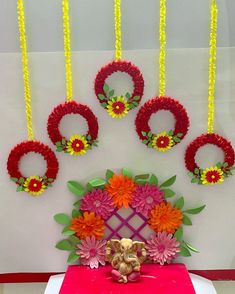 an arrangement of flowers and wreaths on display in front of a white wall with red table cloth