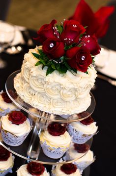 a three tiered cake and cupcakes on a black table with silverware