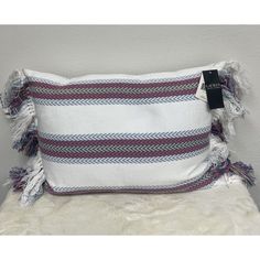 a white and red pillow with fringes on it, sitting on a fur rug