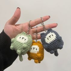 three crocheted keychains in the shape of cartoon characters are being held by someone's hand