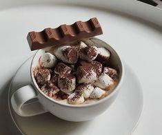 a cup filled with hot chocolate and marshmallows on top of a white plate