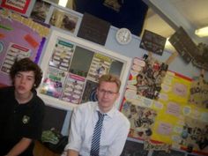 two men sitting next to each other in front of a bulletin board