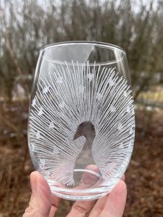 a hand holding up a wine glass with a bird in it's center and trees in the background