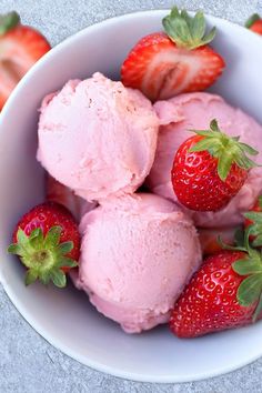 three scoops of ice cream and five strawberries in a white bowl on a wooden table