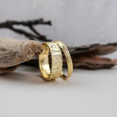 two gold rings sitting next to each other on top of a piece of driftwood