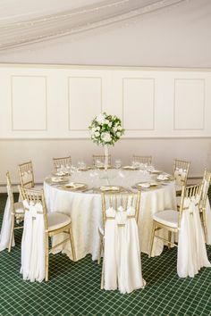 the table is set with white linens and gold chairs for guests to sit at