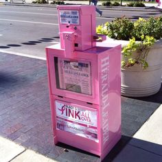 a pink newspaper dispenser sitting on the sidewalk