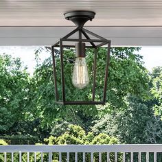 an outdoor light fixture hanging from the ceiling over a porch with trees in the background