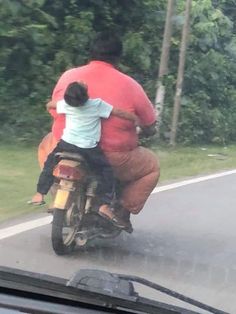 a man riding on the back of a motorcycle down a road next to a forest