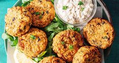 some crab cakes are on a plate next to a small bowl of ranch dip and lettuce