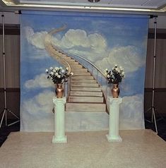 two vases with flowers on them are sitting in front of a wall painted with a stairway